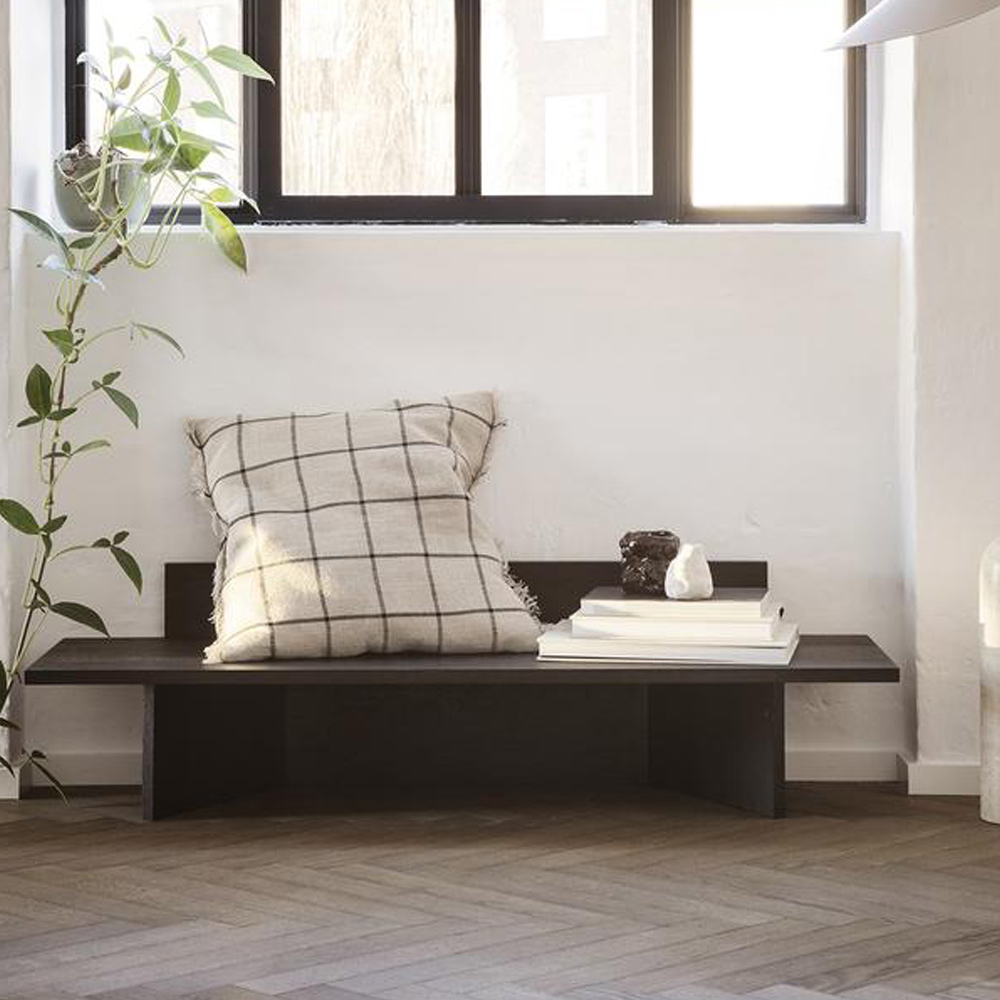 Karriert gemustertes beiges Calm Kissen auf einer dunklen Bank. Das ist Skandinavischer Wohnstil Farben.