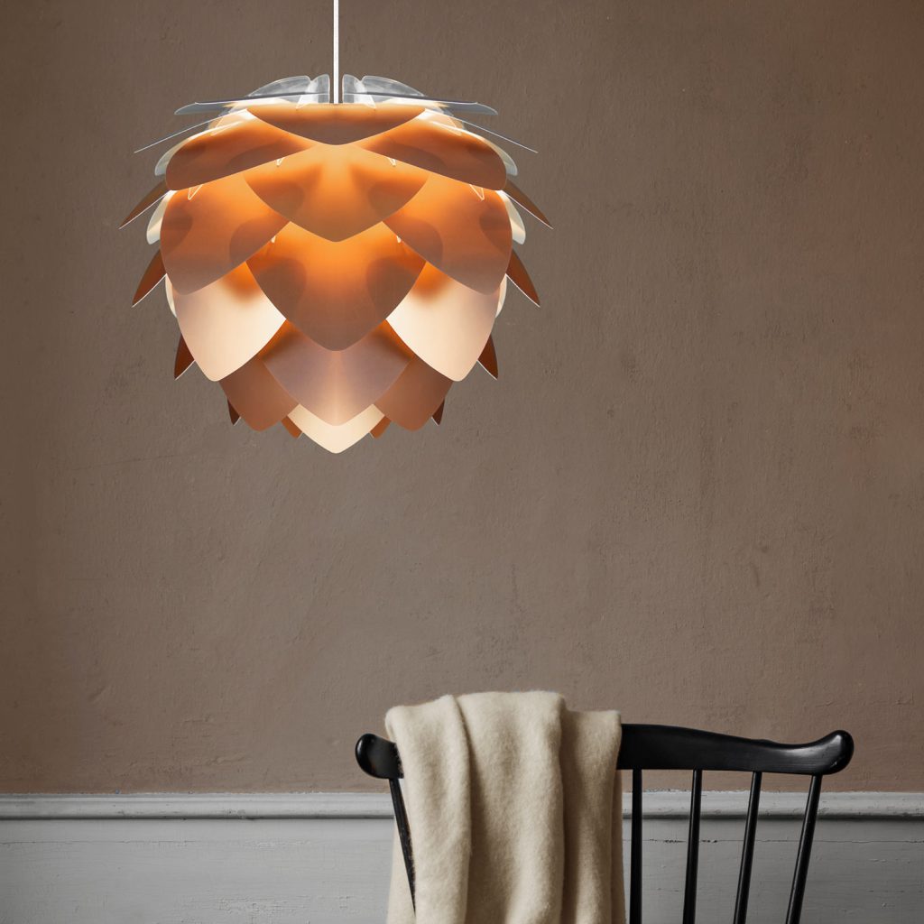 Die kupferfarbene Umage Silvia Pendelleuchte verströmt ihr schimmerndes Licht über einem schlichten schwarzen Stuhl.