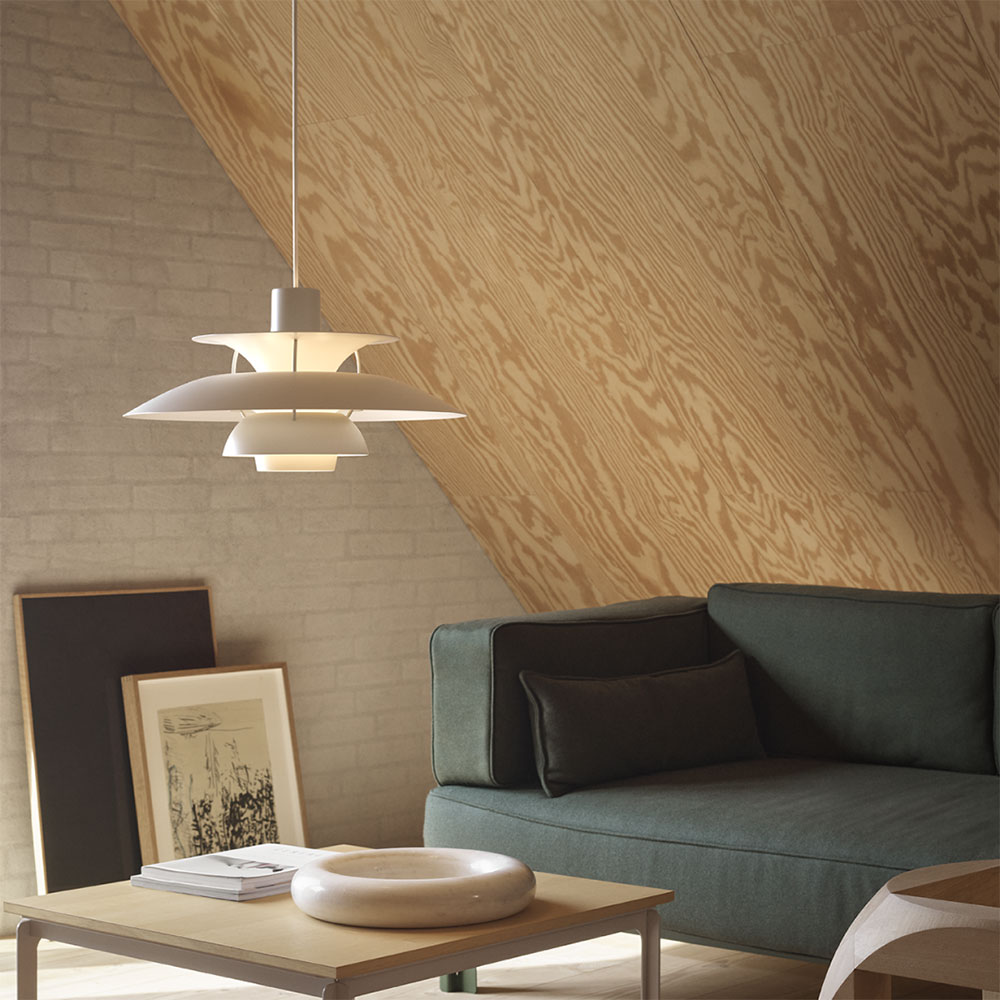 Hygge-Momente kreiert die PH5 auch im Wohnzimmer. In Weiß harmoniert die Poulsen Leuchte perfekt mit dem dunkelgrünen Sofa und der Dachsräge aus hellem Holz.