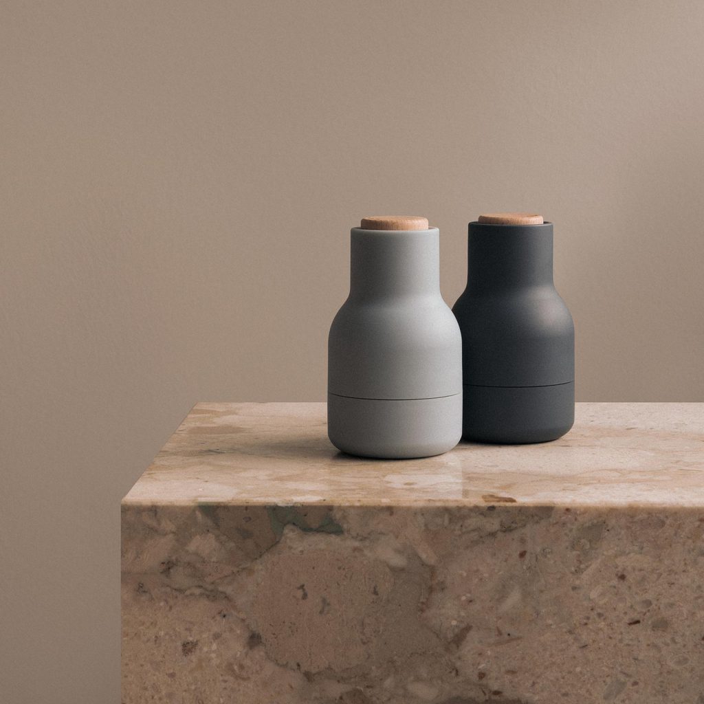Zwei Audo Bottle Grinder Mini Gewürzmühlen in Hellgrau und Schwarz auf einer Marmor-Küchenplatte.