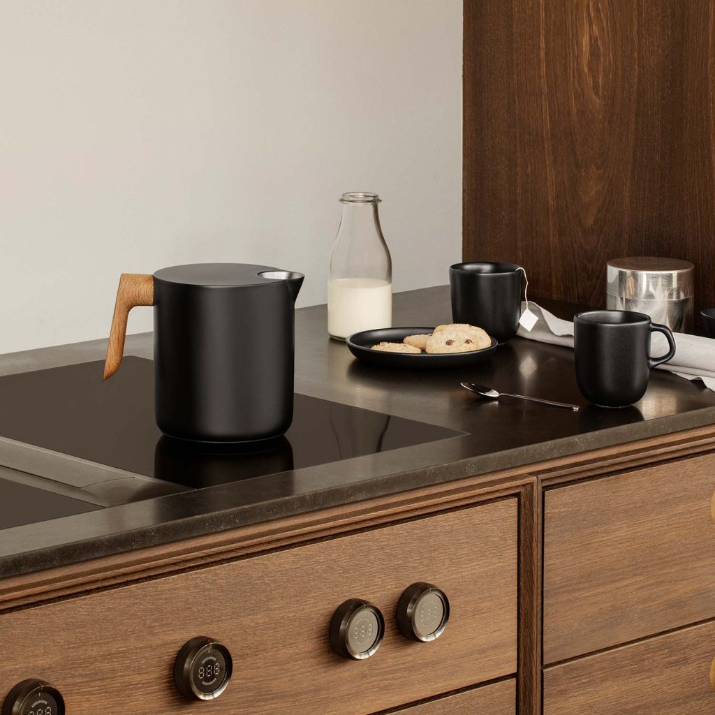 Der elegante Eva Solo Nordic Kitchen Wasserkessel in Schwarz mit Holzgriff auf einem Induktionsherd.